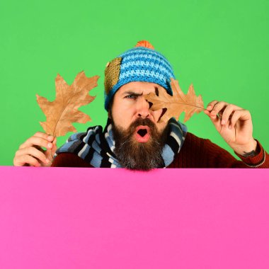 Şapkalı adam gözlerini meşe yapraklarıyla kapar.