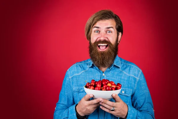 快乐的大胡子男人和甜樱桃。早餐吃樱桃。快乐的男性嬉皮士拿着新鲜的浆果。富含维生素的水果。只有有机食品。节食和健康的生活方式 — 图库照片