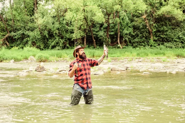 Horgász férfi hobbi. Brutális ember gumicsizmát visel a folyó vizében. Hétvégi elfoglaltság. Halászfelszerelések. Hal a horgon. A halászat megköveteli, hogy figyelmesen és teljes mértékben jelen legyél a pillanatban. — Stock Fotó