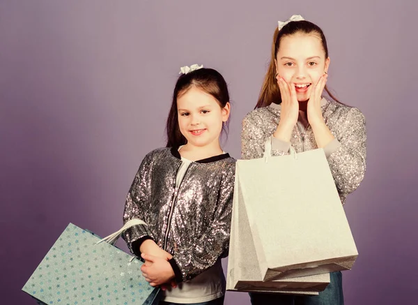 女の子姉妹のお友達でショッピングバッグバイオレット背景。ブラック・フライデー。販売と割引。買い物の日だ。子供用の荷物だ。子供服。何か新しいものを発見。買い物・購入 — ストック写真