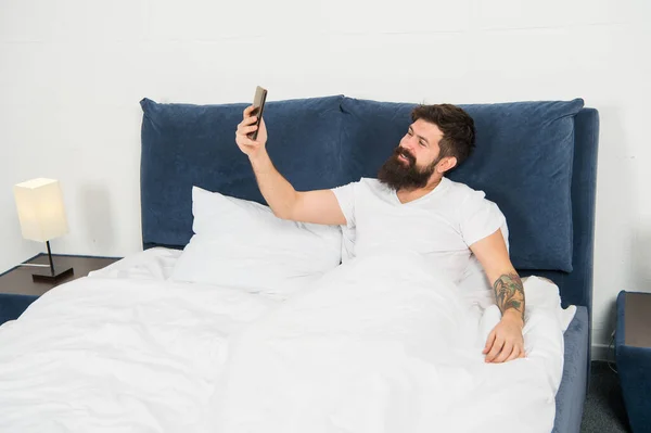 Merhaba canım. Sakallı adam yatakta internette sohbet ediyor. Hippi, kameralı telefona bak. Çevrimiçi toplantı. Mobil cihazda video konferansı. Çevrimiçi video görüşmesi. Akıllı telefon iletişimi. Görsel efektler. Blogger yaşam biçimi — Stok fotoğraf