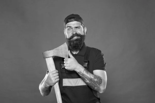 Brutal job. Dismantling and demolition of structures. Bearded lumberjack. Man builder uniform hold axe. Man builder hold ax red background. Renovation concept. Bearded handyman. Brave worker