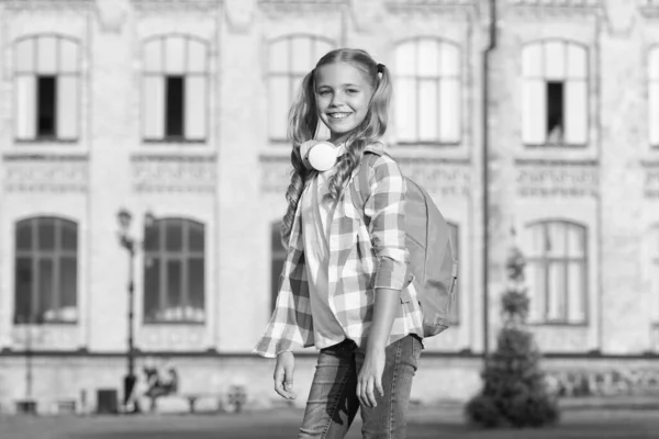 Menina pequena usar camisa xadrez. criança com fone de ouvido ao pôr-do-sol. Primavera de criança e moda de verão. infância feliz. e-learning com ebook. tecnologia moderna. amante de música alegre com mochila — Fotografia de Stock