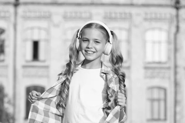 Szczęśliwa uczennica nosi słuchawki. mała dziewczynka casual stylu outdoor. Wiosenne wakacje właśnie się zaczęły. jej ulubiona letnia playlista. dziecko słucha muzyki. uśmiechnięty dzieciak słuchający audiobooka — Zdjęcie stockowe
