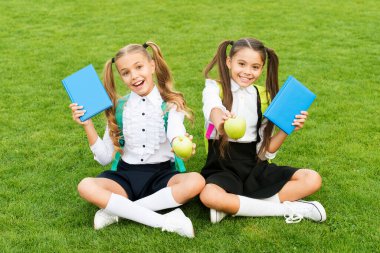 Çocuklar için beslenme eğitimi. Mutlu çocuklar dışarıda elma ve kitap tutarlar. Küçük çocuklar yeşil çimlerde okul tatilinin tadını çıkarıyorlar. Okul çocukları atıştırmalık molası verir. Sağlıklı beslenme. Okula geri dön.