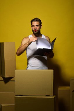 Sakallı adam ayakta duruyor ve sarı arka planda okuyor.