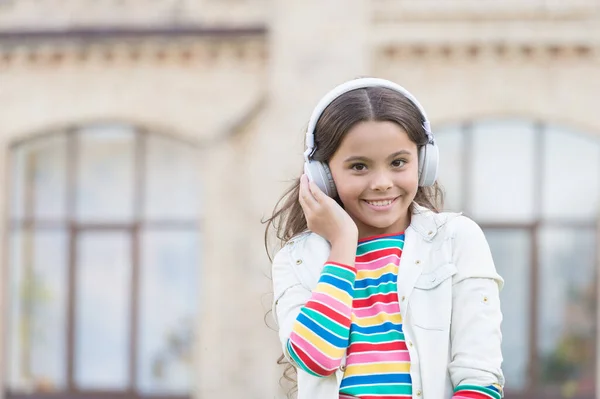 こんにちは。小学生の女の子は屋外で音楽を聞く。学校に戻って。小さな女の子は近代的な技術を使う。おしゃれなヒップスターの衣装を着た幸せな女子高生。子供の頃の幸せ。デジタルイヤホンの子供は — ストック写真