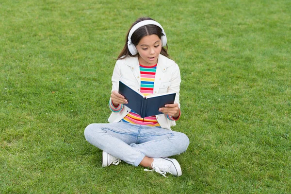 Ontwikkeling van de verbeelding. Schattig meisje leest boek. Gelukkig kleuter meisje met boek op schoolplein. terug naar school. hardwerkende kind met koptelefoon. begrip onderwijs en lezen. een schrijver zijn — Stockfoto