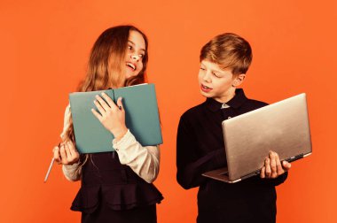 Evde eğitim. Küçük çocuklar kitap ve dizüstü bilgisayarlarını kahverengi arka planda tutarlar. Okuldaki küçük kız ve oğlan. Zorunlu eğitim. Okul ve eğitim için. Çevrimiçi kurslar ve e-öğrenme. Okul yılları.