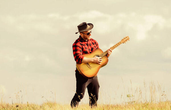 Play beautiful melody. Country music concept. Guitarist country singer stand in field sky background. Inspired country musician. Hiking song. Handsome man with guitar. Country style. Summer vacation