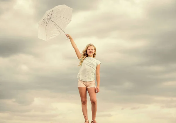 Bambino spensierato all'aperto. Previsioni meteo. Pronti per qualsiasi tempo. Il tempo cambia. Aria fresca. Ragazza con ombrello cielo nuvoloso sfondo. Libertà e freschezza. Concetto anti gravità. Godere di facilità — Foto Stock