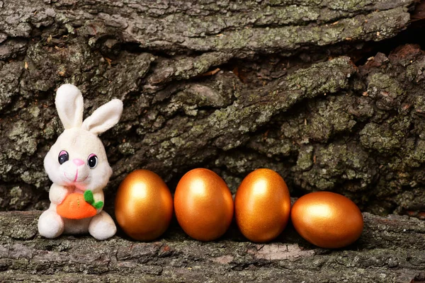 Jouet de lapin, oeufs de Pâques dorés sur fond d'écorce d'arbre — Photo