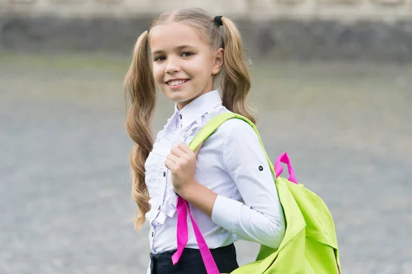 Розумний чудовий... повертається до школи. дитина в уніформі несе шкільну сумку. концепція освіти. розвиток дитинства. щаслива дівчина має милу посмішку. щаслива дівчина дошкільного віку з рюкзаком на шкільному подвір'ї — стокове фото