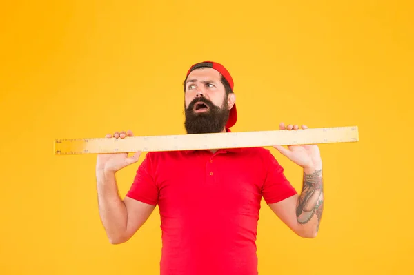 Dimensioni del pacco. Operaio dell'ufficio postale con righello. Grosse dimensioni. Strumento di misura. Uomo reggente su sfondo giallo. Un uomo barbuto che si prepara alla matematica. Hipster uomo in cappuccio con grande strumento di misura — Foto Stock