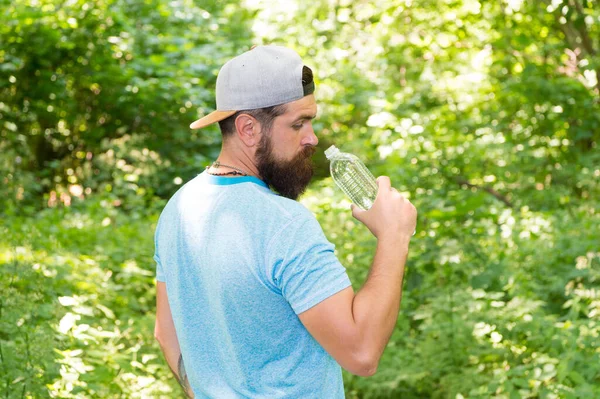 Varje klunk räknas. mogen kille i hatt. Törstig hipsterresenär. dricksvatten i skogen utomhus med solnedgång natur på bakgrunden. Skäggig man med vattenflaska. fitness porträtt av skäggig man — Stockfoto