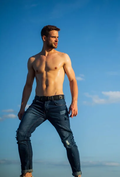 Torso desnudo muscular. Seis maços de peito muscular. Homem ao ar livre fundo céu azul. Tendências de verão. Conceito de beleza masculina. Dia quente. Atletismo bonito macho usar calças jeans. Corpo muscular. Modelo de aptidão — Fotografia de Stock