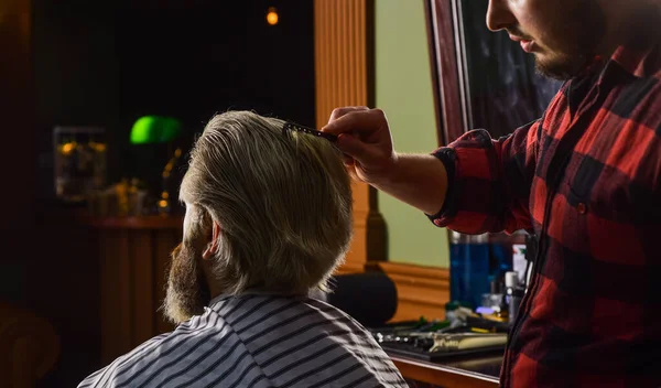 Un cliente hipster che si taglia i capelli. Barbiere con forbici e cliente. Un tipo con i capelli biondi tinti lunghi da vicino. Non tagliarti i capelli. Barbiere lavora su acconciatura per barbuto uomo barbiere sfondo — Foto Stock