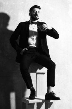 Sakallı adamın elinde matara, stüdyo duvarında ciddi bir yüz var.