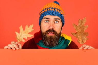 Şaşırmış yüzlü adam turuncu arka planda kalın bir şapka takıyor.