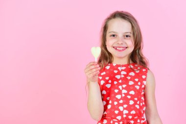 Mutlu çocuk pembe arka planda kalp şekeri tutuyor