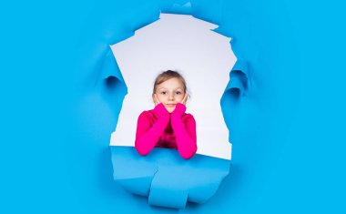 Kadın kuaför salonu. Güzellik ve moda. Mutlu çocuğun sıradan bir görünüşü var. Modayı takip eden çocuğun mutlu bir çocukluğu var. Mavi arka planda küçük bir kız. Neşeli duyguları olan çocuk.