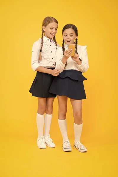 Uniforme escolar meninas usando smartphone. As alunas usam telefone celular ou smartphone para compartilhar fotos. Aplicativo escolar smartphone. Internet é um recurso maravilhoso, mas o acesso a ela tem perigos para as crianças — Fotografia de Stock