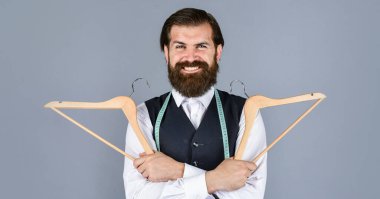 O çok mutlu. Resmi yelek giymiş yakışıklı bir adam. İş modası için gardırop. Giysi ve alışveriş. Askıda asılı duran şık erkek kıyafetleri. Terzi elinde bir askı tutuyor.