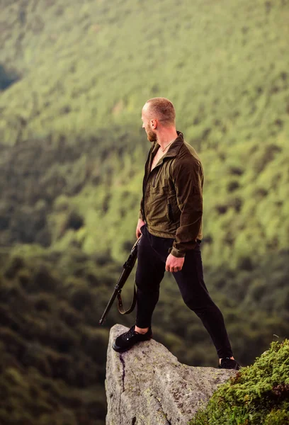 Hunter caçador furtivo à procura de vítima. Caçador com rifle ambiente natureza. Caça ilegal. Conceito de caça furtiva. Poacher stand on edge of cliff. Homem brutal caçador furtivo com arma paisagem natural fundo — Fotografia de Stock