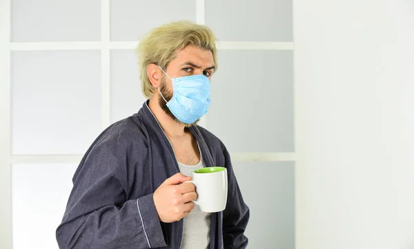 De man drinkt koffie met een medisch masker. 's Ochtends thuis op Coronavirus zelfisolatie. pandemische quarantaine. Anti-virus masker. Maskers om te beschermen tegen virussen. Man draagt masker om te beschermen tegen virale infectie — Stockfoto