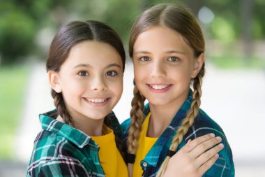 Birbirimizi seviyoruz. Moda kıyafetleri içinde gülümseyen iki genç hippi kız. Dışarıda poz veren kaygısız çocuklar. Pozitif modeller. Sıradan hippi kıyafeti. Mutlu kız kardeşlerin portresi. Küçük çocuklar tişörtlü kızlar