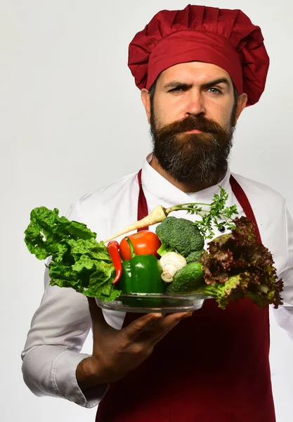 Cook with confident face in burgundy uniform holds salad ingredients