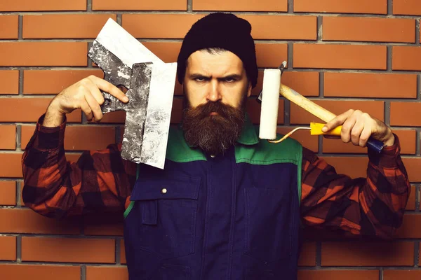 Homem pintor barbudo segurando várias ferramentas de construção com rosto sério — Fotografia de Stock