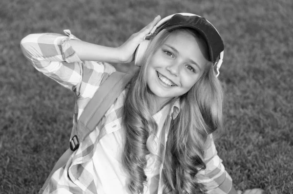 楽しい時間だ。子供のヘッドフォンは音楽を聞く。女の子のヘッドフォン音楽を聞いて。教育用ポッドキャスト。あらゆる瞬間をお楽しみください。屋外でリラックスしながら音楽を聴く。子供の女の子は音楽を楽しむ緑の草の牧草地 — ストック写真
