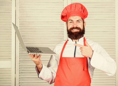 Aşçılık okulu. Şapkalı ve önlüklü hippi internetten ürün alıyor. İnternetten alışveriş. Teslimat servisi. Aşçı adam internette yemek pişiriyor. Market çevrimiçi. Mutfakta şef dizüstü bilgisayar.