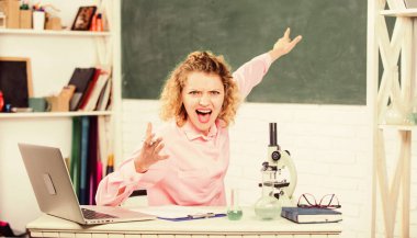 Masasında dizüstü bilgisayarı ve okul gereçleri olan bir kadın öğretmen ya da öğrenci. Sınıfın yazı tahtası geçmişinde duygusal kadın öğretmen eğitmeni. Duygusal kontrol için. Duygusal insanlar konsepti