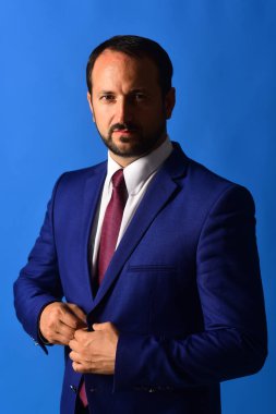 Lider koyu mavi arka planda ceketin düğmelerini açar.