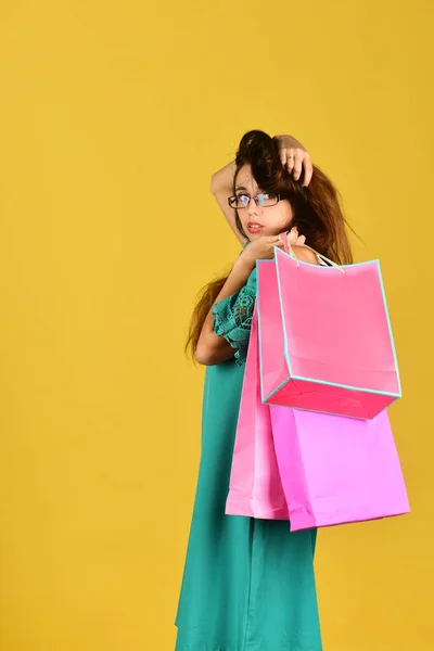 Lány áll a sárga háttér, tartja rózsaszín bevásárló táskák — Stock Fotó