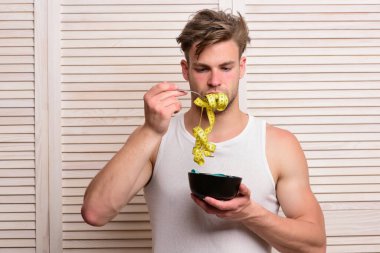 Kolsuz tişörtlü, dağınık saçlı ve mezura yiyen adam.