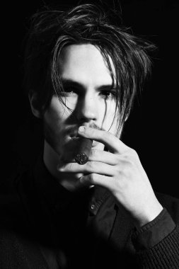 Ciddi sakallı bir adam siyah stüdyo arka planında puro içiyor.