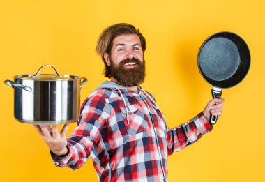 Gizli bileşen neşe. Tencereli adam. Adam yeni marka tavayı tutuyor. Mutfak gereçleri. Mutfaktaki aşçıda tencereyi pişirirken. Yemek hazırlamak ve yemek pişirmek. Mutfak aletleri.