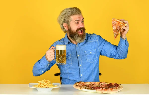 Frytki. Facet w barze pije piwo i je pizzę. Zdrówko. oglądanie futbolu w telewizji. Amerykańskie fast foody. szczęśliwy brodaty mężczyzna z pizzą i piwem. włoska żywność — Zdjęcie stockowe