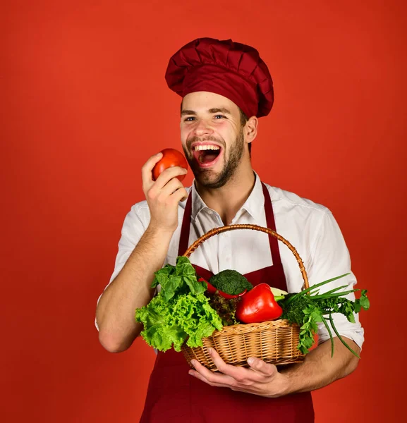 Hombre con barba mordiendo tomate sobre fondo rojo —  Fotos de Stock