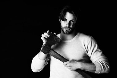 Sakallı ve dikkatli bakışlı adam yaşlı paslı baltayı tutuyor.