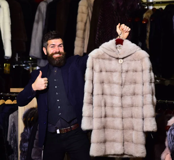 Luxury clothing concept. Guy holds beige furry coat in shop.