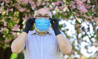 Tamamen korunmuş görünüyor. Koronavirüs karantinasında çiçek kokusu alıyorum. Salgın sırasında önlemlere dikkat edin. sağlıklı bir hayat. Çiçek açan pembe sakura parkında maske takın. Sakura 'daki koruyucu maskeli adam.