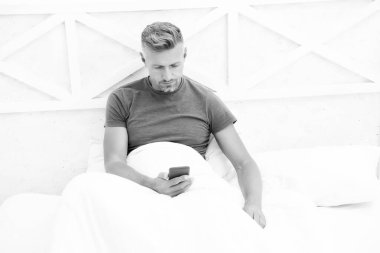 Çevrimiçi iletişim. Olgun bir adam yatakta cep telefonu kullanır. Mobil iletişim. Hücresel iletişim. İletişim teknolojisi. Modern hayat. Kendini izole et ve karantina altına al. Evde kal. Günaydın.