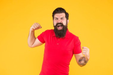 Zafer ve başarı. Sıradan giyinmiş sakallı adam kutlama yapıyor. Mutluluk ve neşe. Kazanan ve kazanan. Neşeli adam. İç enerji. Başarı için motive. Mutlu adam başarısını sarı arka planda gösterir.