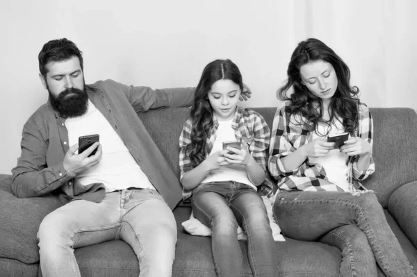 Online family. Family spend weekend online. Child little girl use smartphone with parents. Family surfing internet. Mom dad and daughter relaxing on couch. Family leisure. Play game application