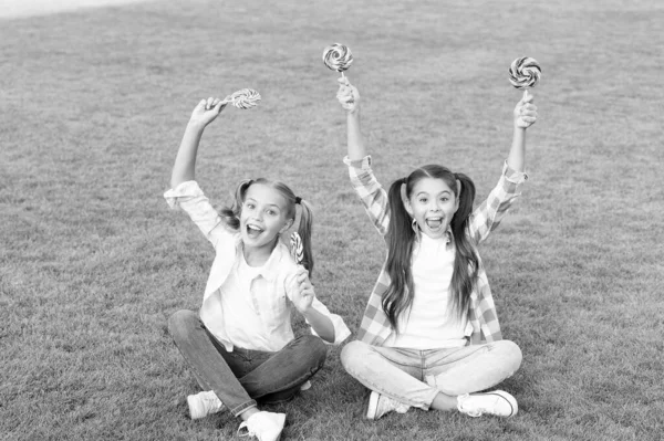 Feliz, bonito e doce. Meninas felizes comer pirulitos grama verde. Loja de doces. A divertir-se ao ar livre. Lazer e tempo de descanso. Férias. Feliz e brincalhão. Ser positivo — Fotografia de Stock