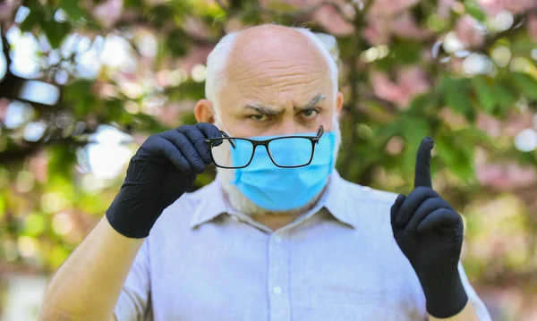 Beschermen en tegen virusinfectie. Beperk de verspreiding van infecties. Senioren geloven desinformatie over covid-19. Senior man draagt gezichtsmasker en handschoenen buiten. Infectie is in de lucht — Stockfoto